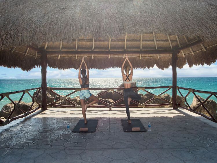 Two women in yoga pose under a shed facing ocean view