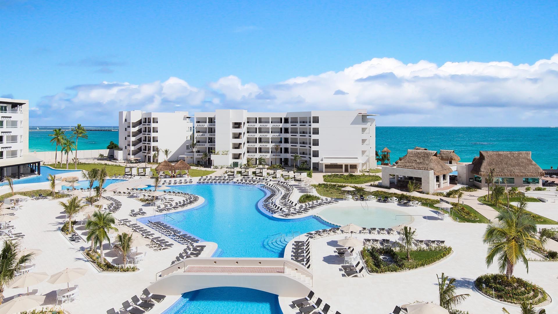 Pool view with resort building, trees and ocean in the background